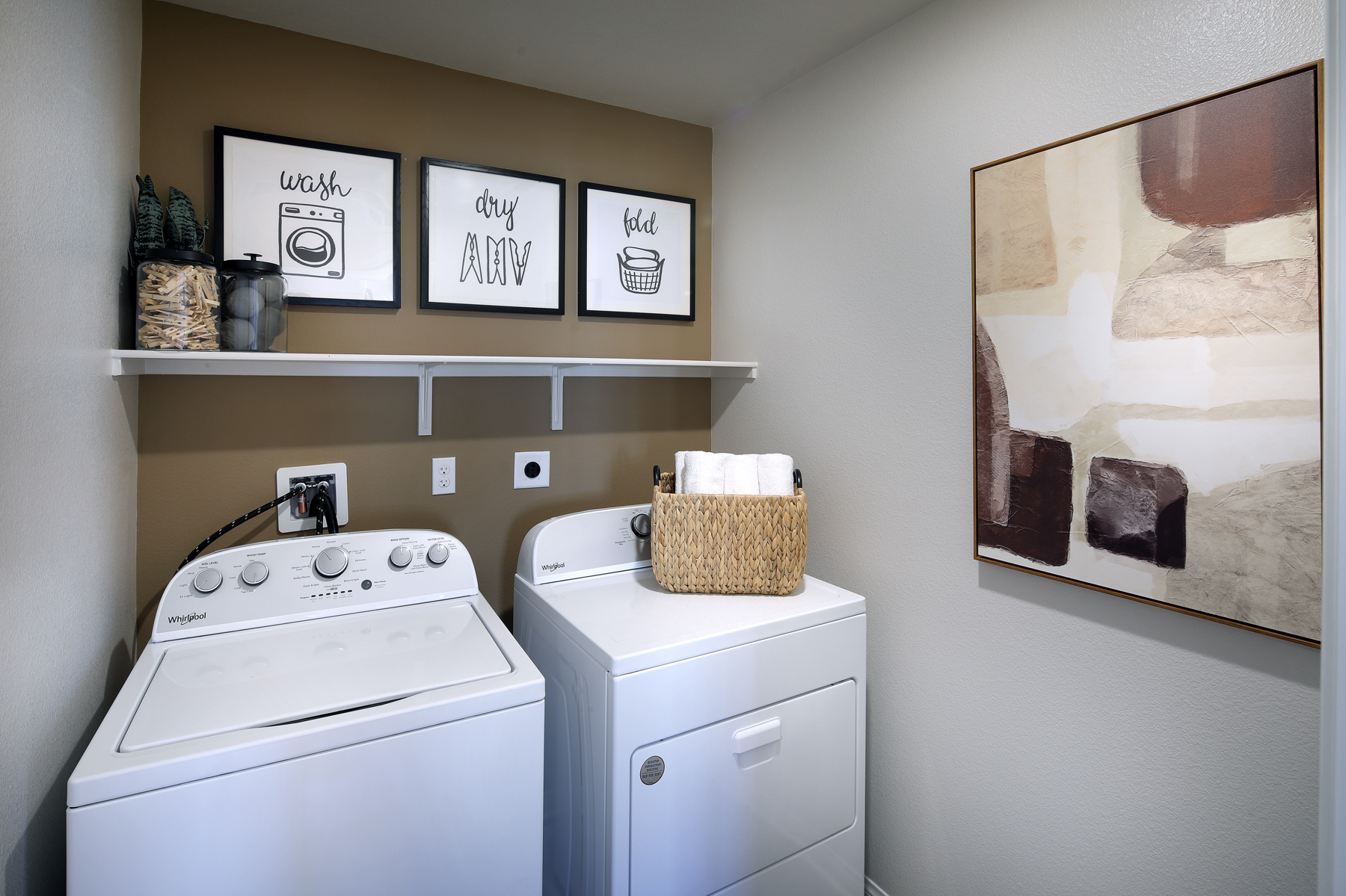 A white laundry room with a shelf and a basket on the wall.
