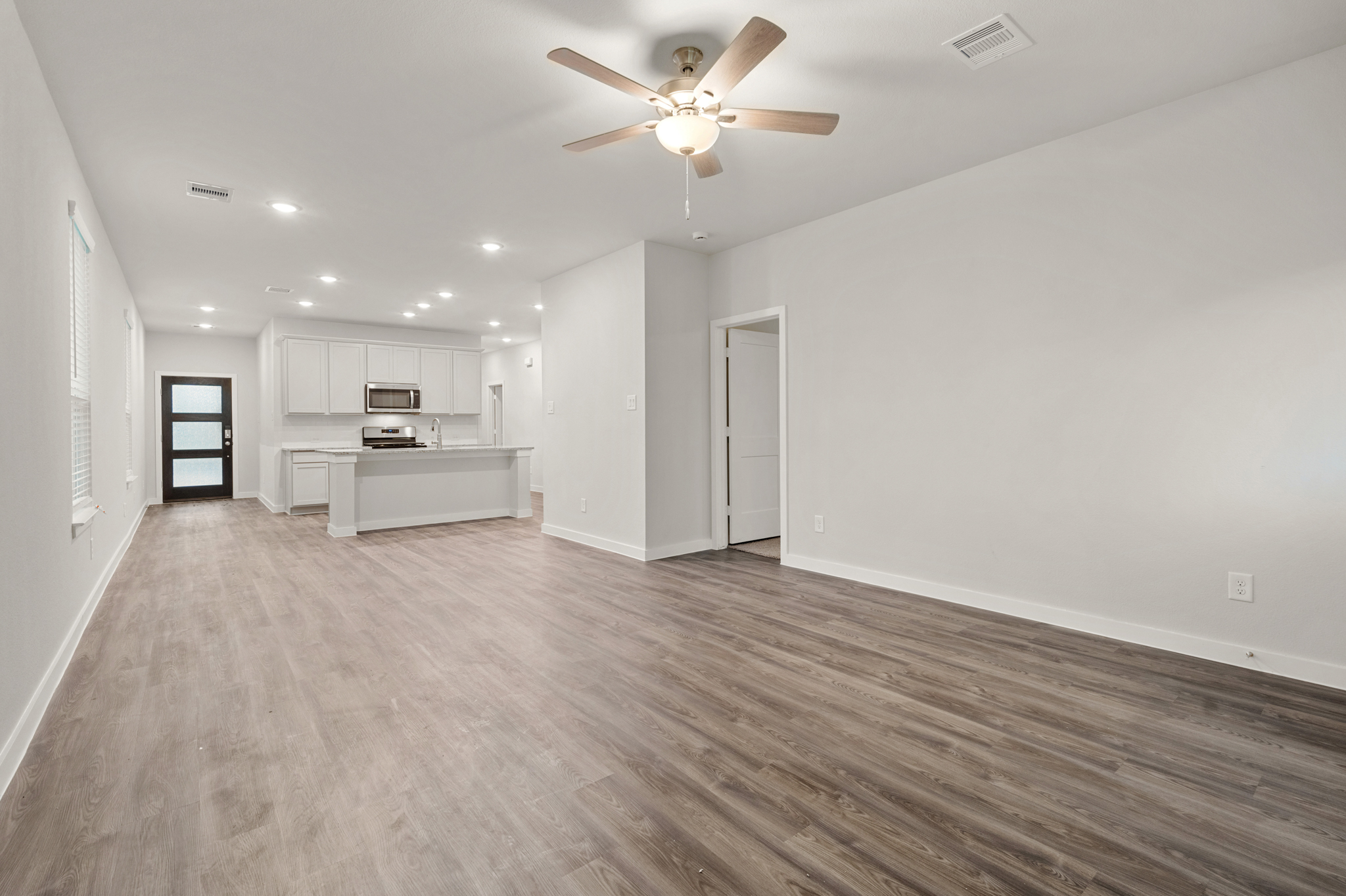 A large empty room with a ceiling fan and a wood floor.