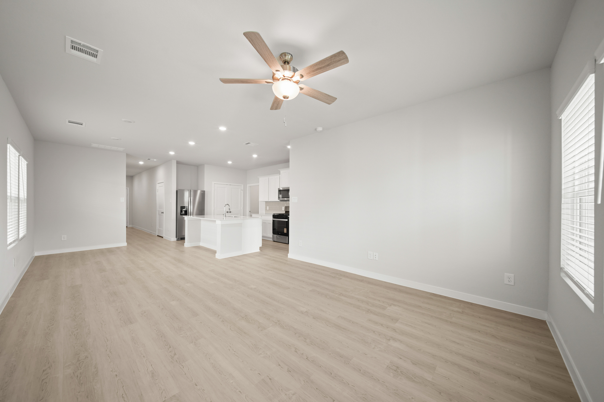 A large empty room with a ceiling fan and a wood floor.