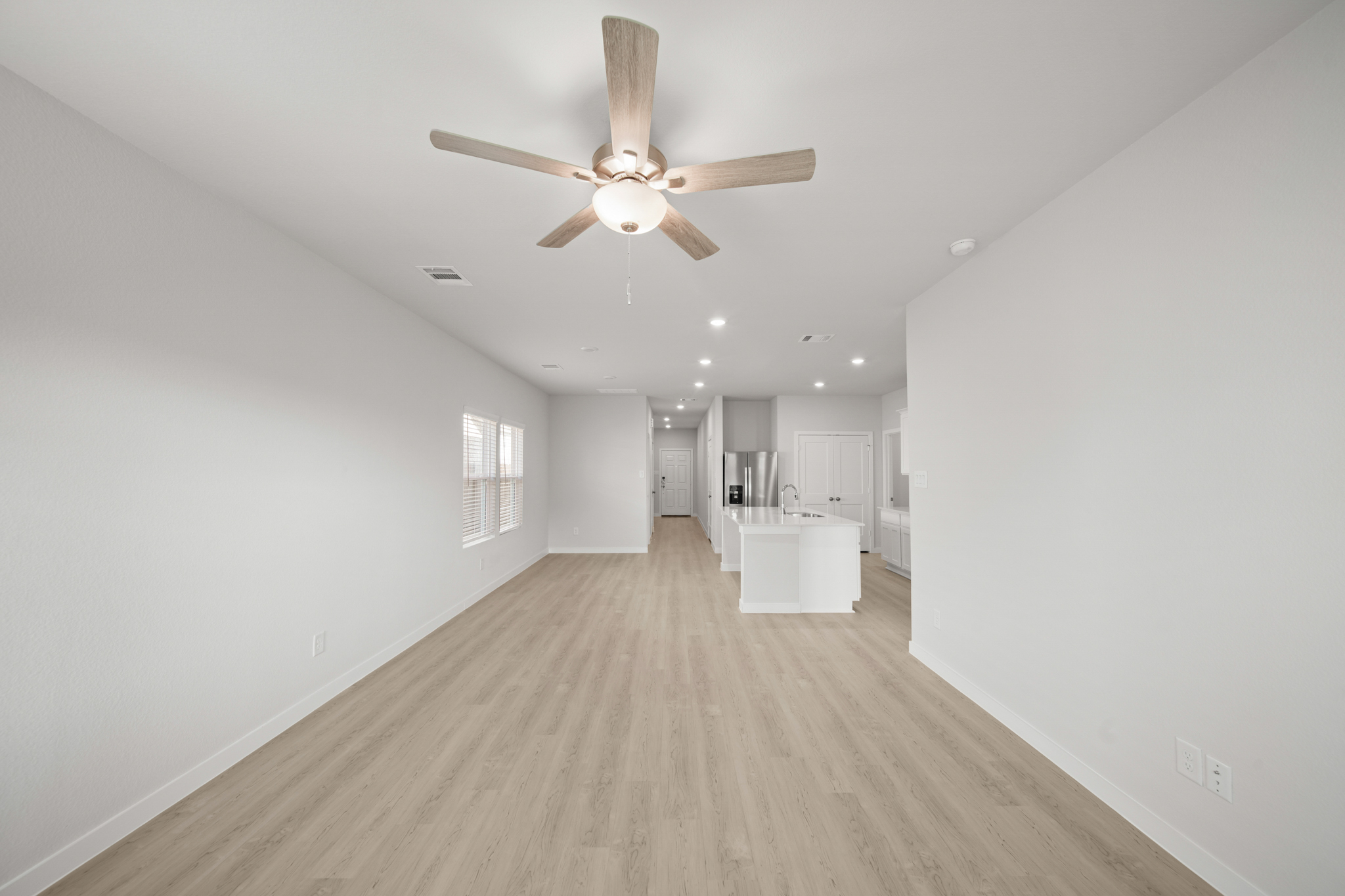 A large empty room with a ceiling fan and a wood floor.