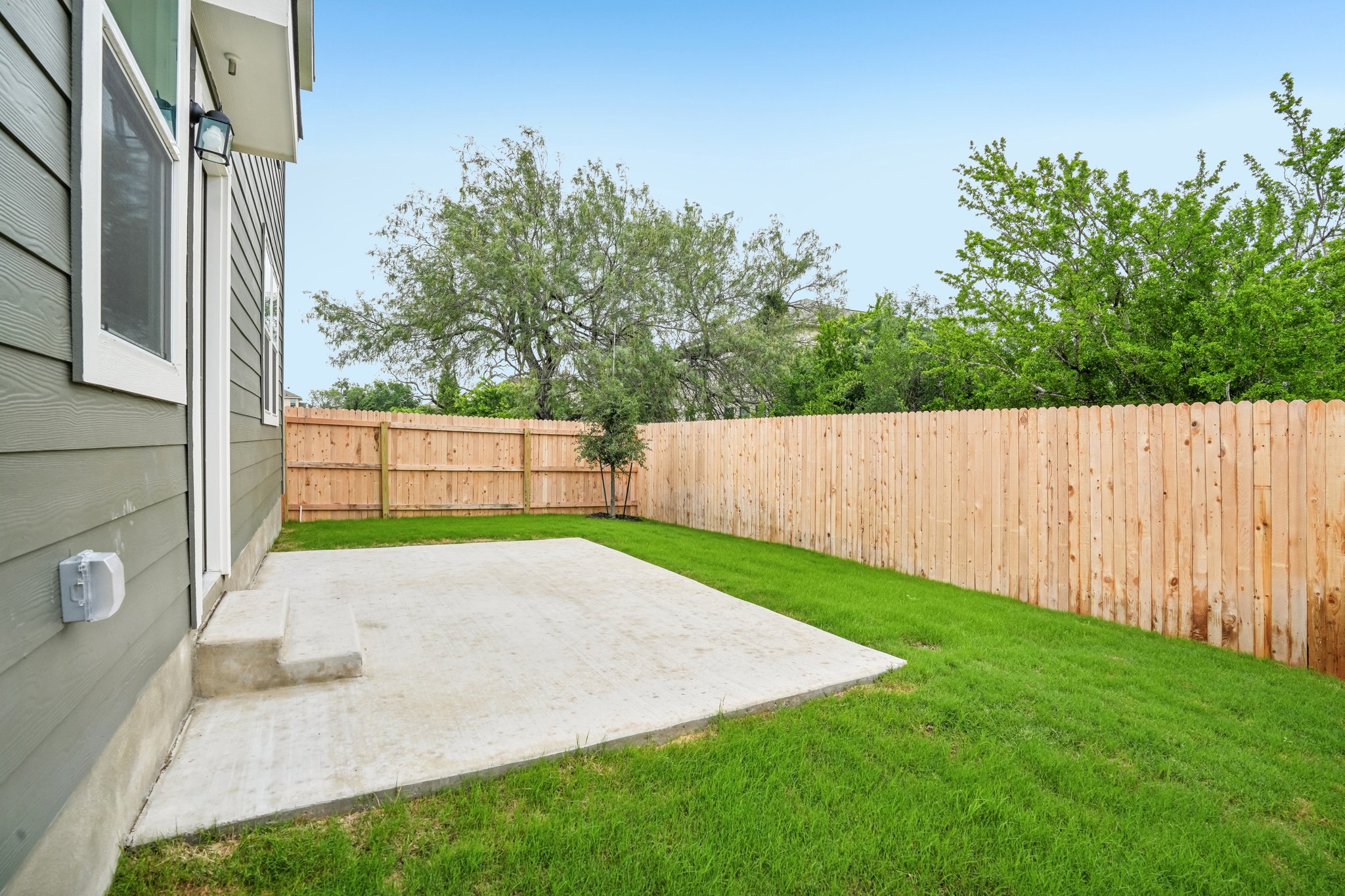 A fenced yard with a house and trees in the background.